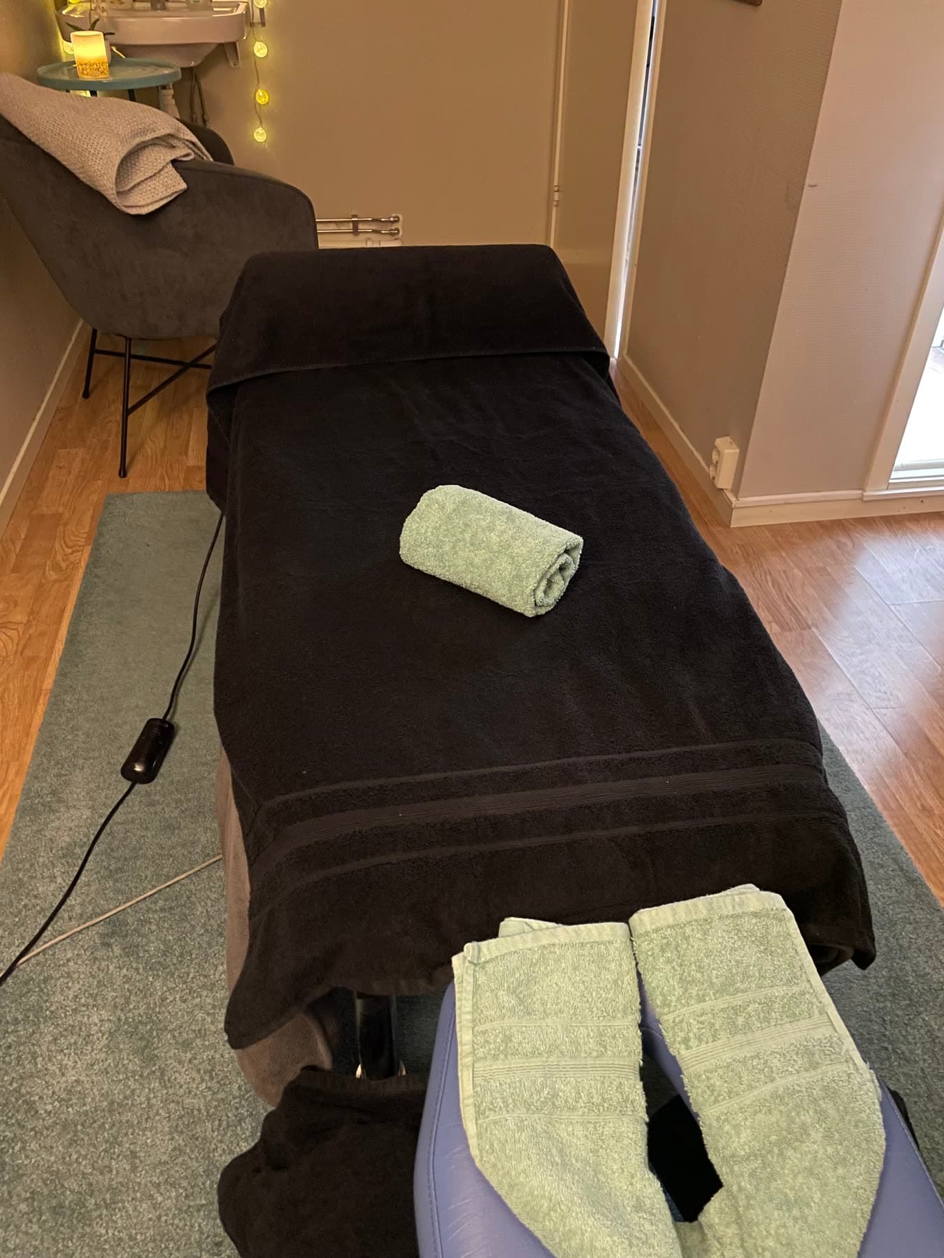 Bäddad behandlingsbänk vid fönstret, med rullad handduk och nackstöd