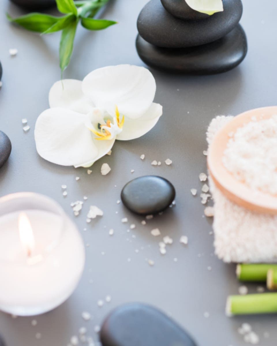 Massagestenar, orkidé, ett tänt ljus och en hoprullad handduk